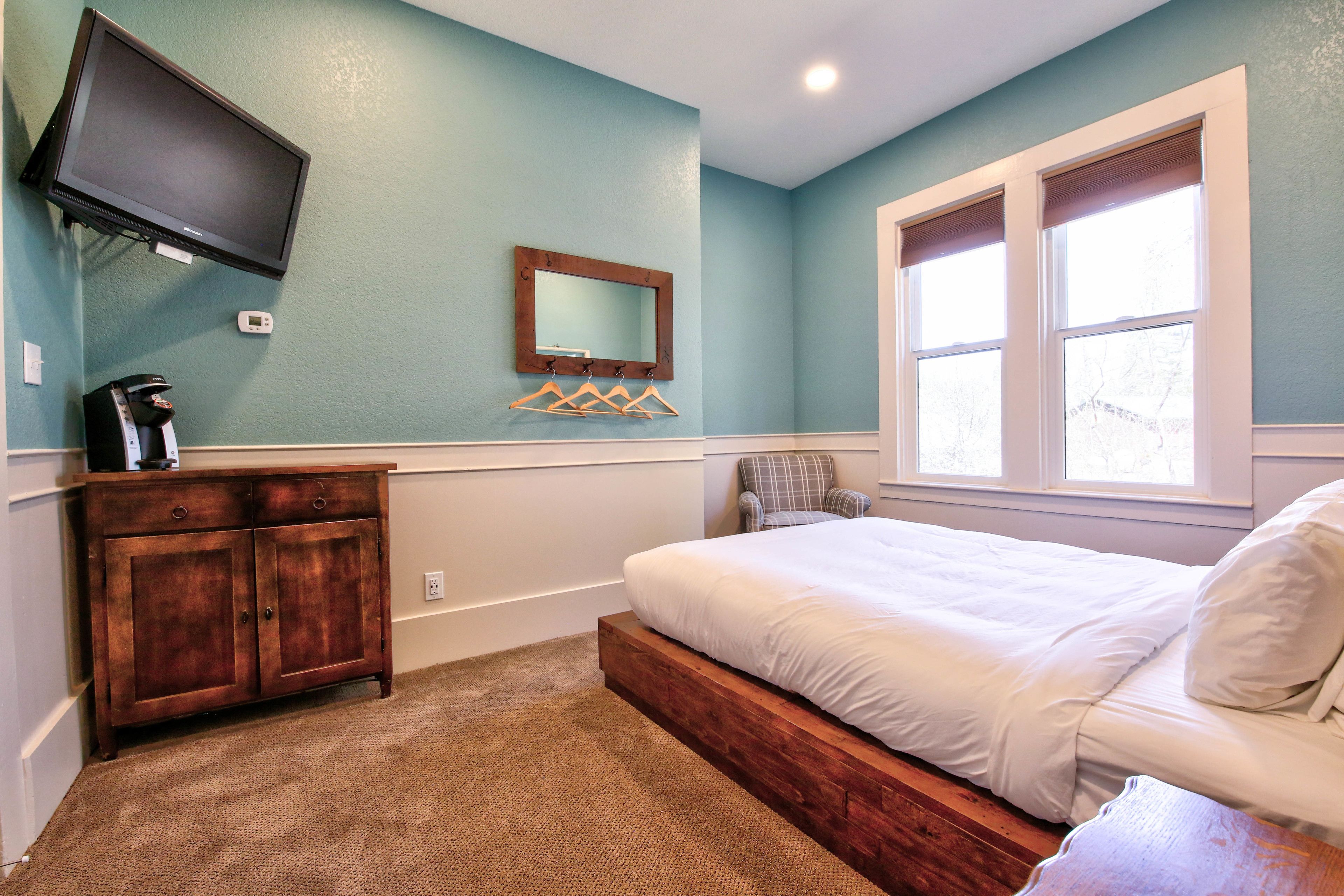 Un dormitorio con cama, cómoda, televisor montado en la pared y ventana.