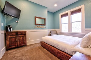 Un dormitorio con cama, cómoda, televisor montado en la pared y ventana.