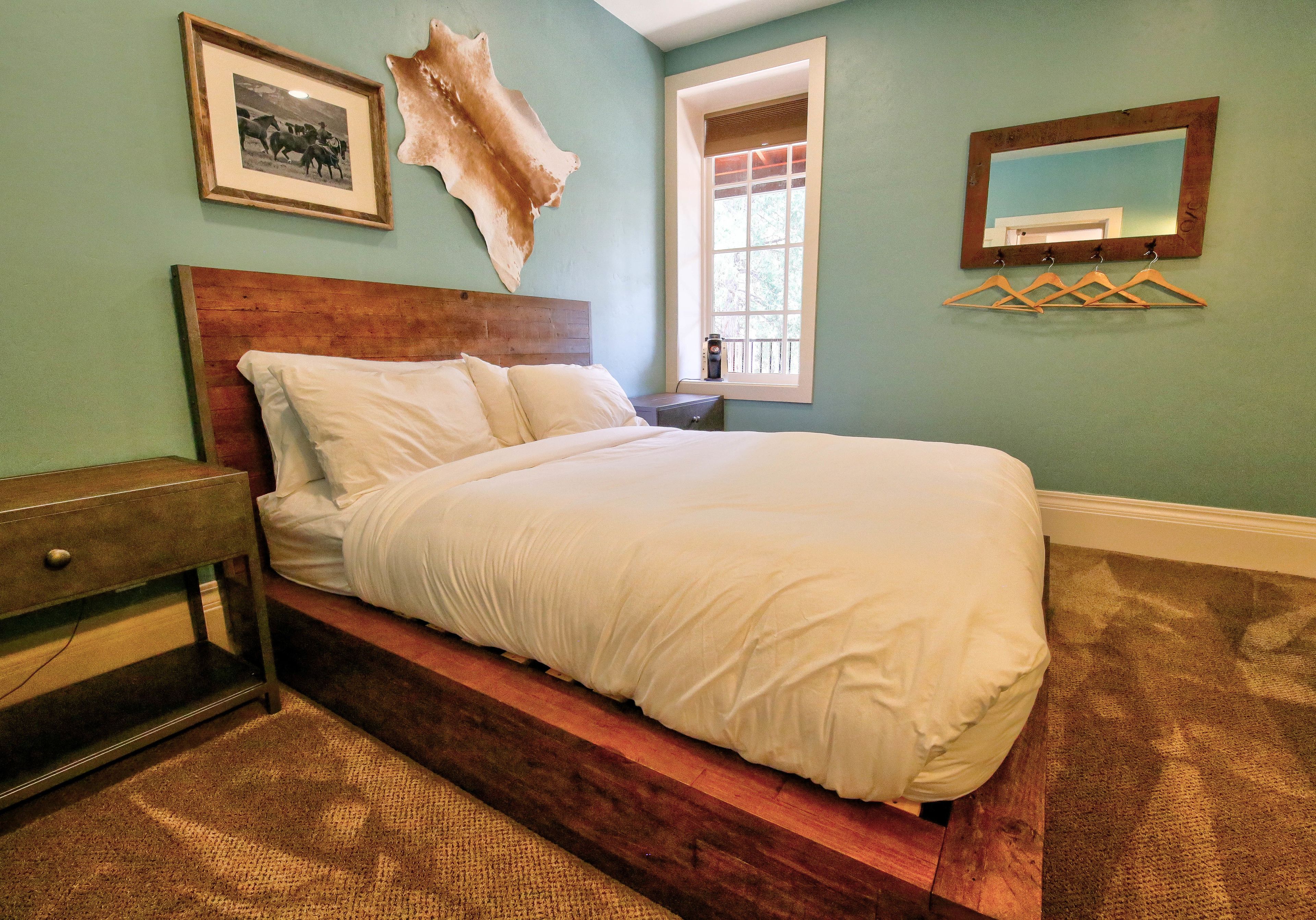 Una camera da letto con un letto in legno, un comodino, un quadro incorniciato, una decorazione a parete in pelle di mucca, una finestra e uno specchio.