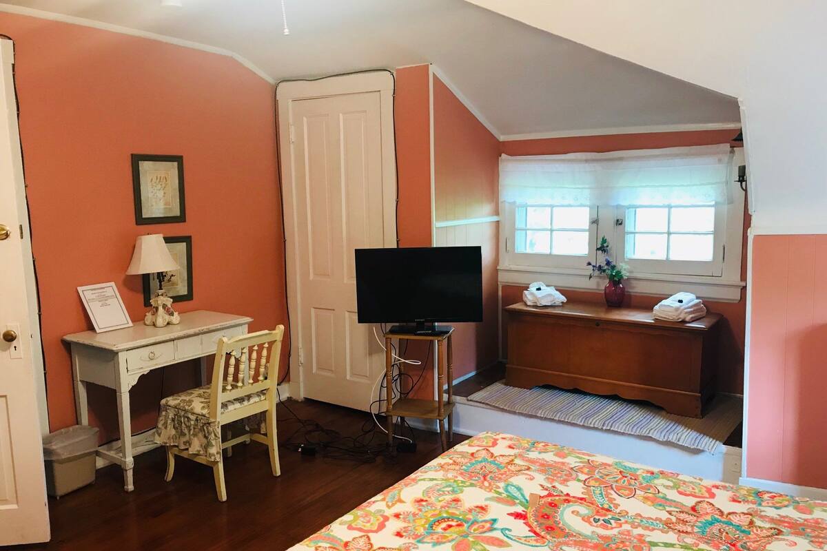 A bedroom with a bed, a desk with a chair, a television, and a window with curtains.