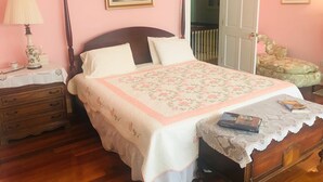Une chambre à coucher comprenant un lit, une table de chevet, une commode, une lampe et une porte donnant sur une autre pièce.