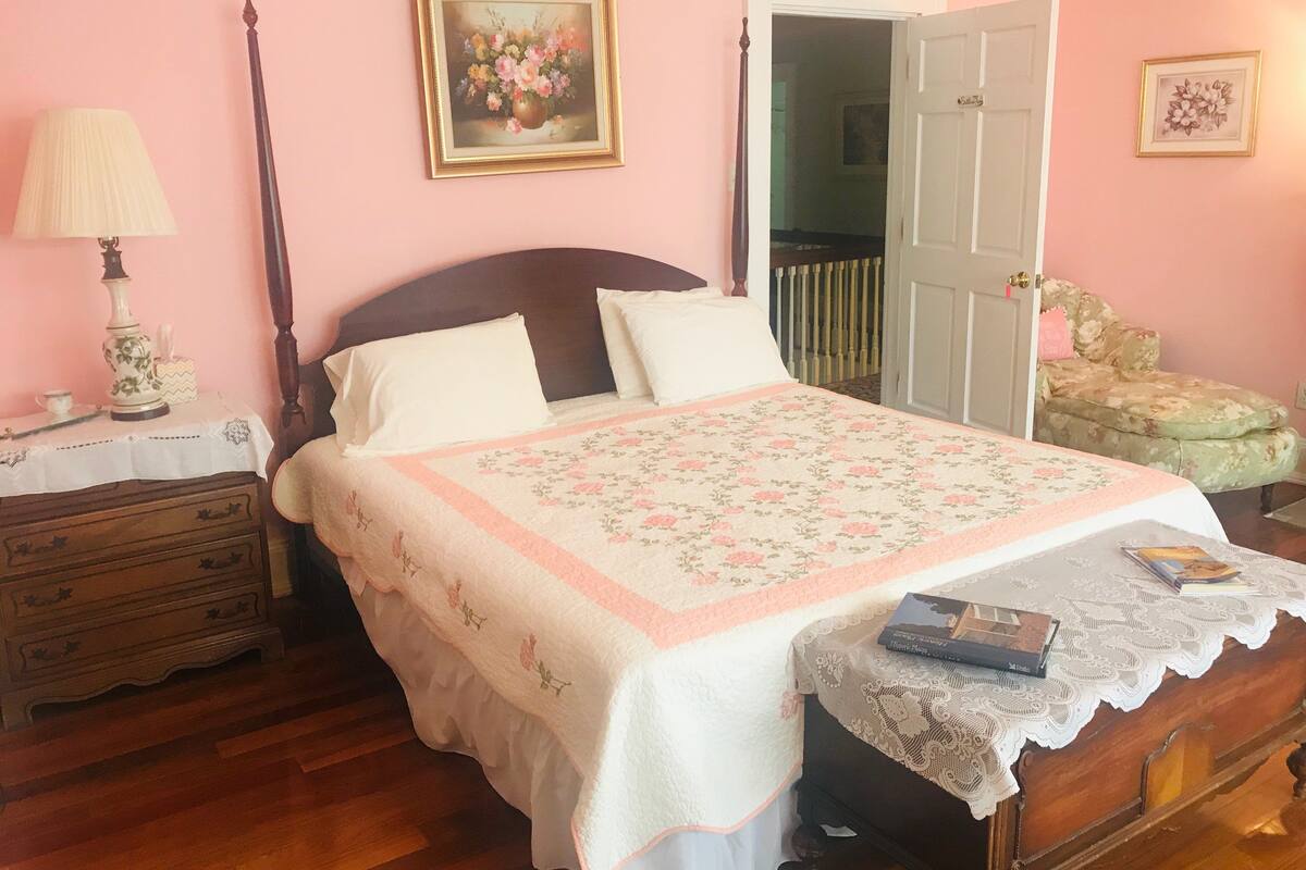 A bedroom with a bed, a nightstand, a dresser, a lamp, and a door leading to another room.