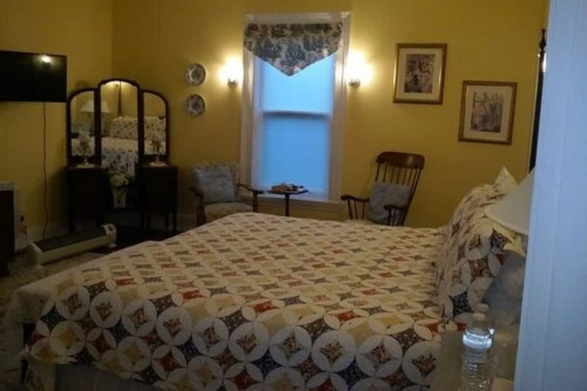 A bedroom with a bed, a chair, a table, a mirror, and a window with curtains.