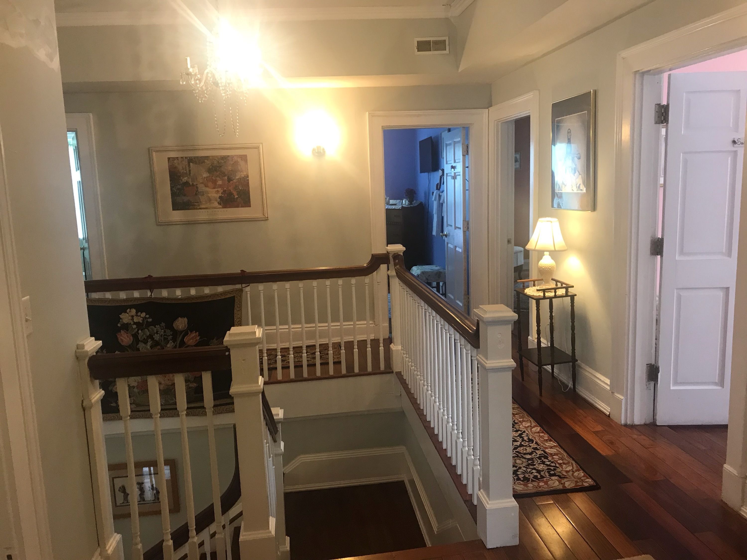 A staircase with white railings and a wooden handrail, leading to a landing with a patterned rug.