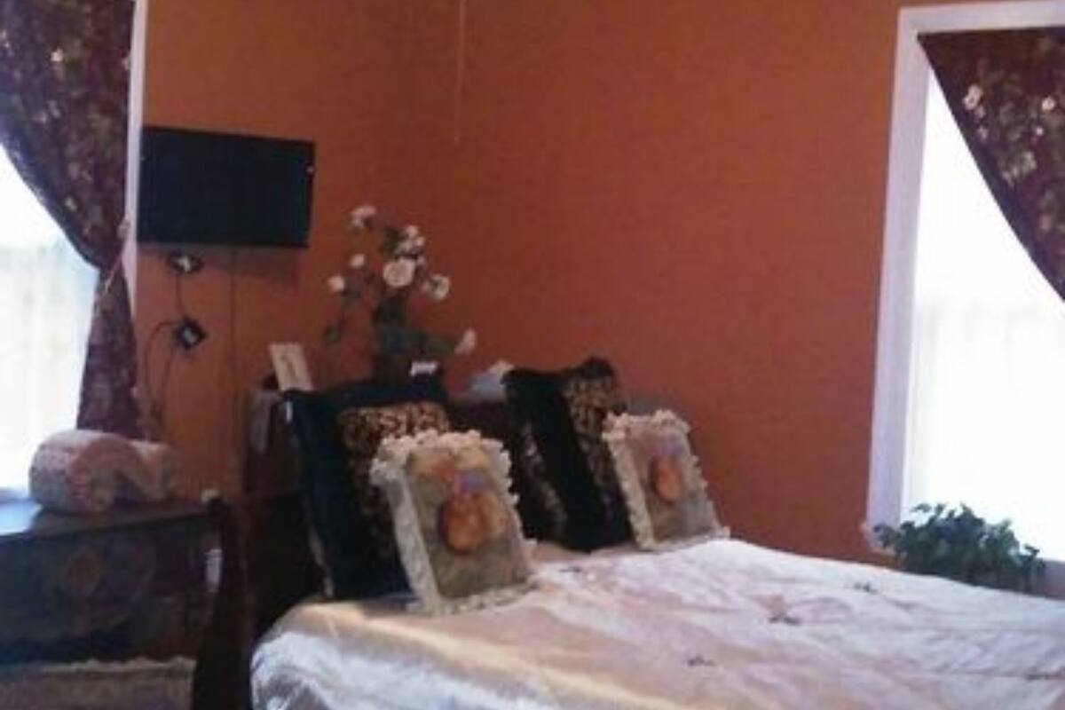 A bedroom with a bed, a ceiling fan, a flat-screen TV, and a window with curtains.