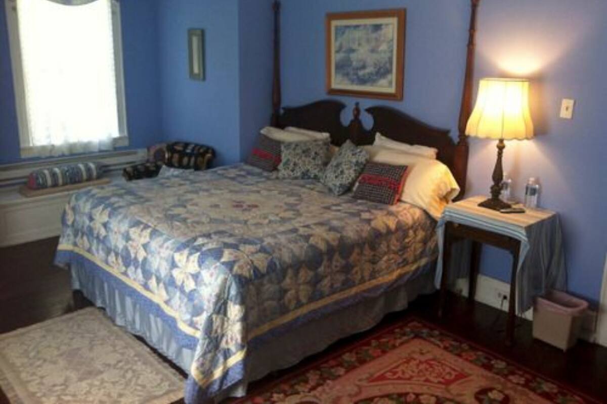 A bedroom with a large bed, a nightstand with a lamp, a window with curtains, and a framed picture on the wall.