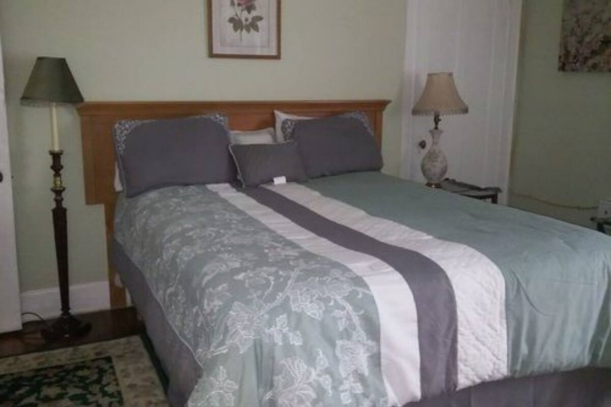A neatly made bed with a headboard, two bedside lamps, and a framed picture on the wall.