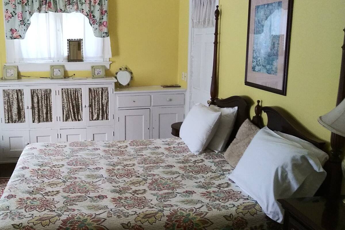A bedroom with a bed, a dresser, a television, and a window with curtains.