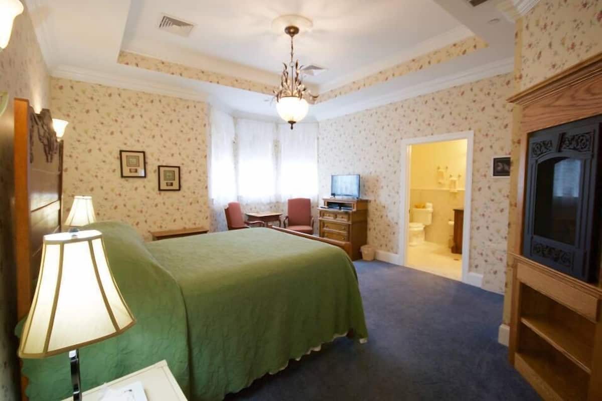 A bedroom with a bed, a desk, a chair, a television, and a bathroom visible through an open door.