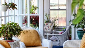 Una habitación luminosa con muebles de mimbre, ventanas amplias y plantas colgantes.