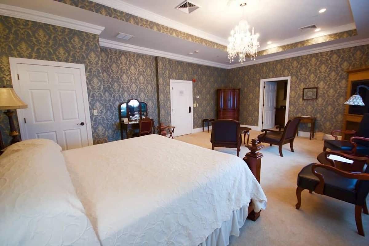 A large bed with a white bedspread, a chandelier, and a wooden cabinet in a room with patterned wallpaper.