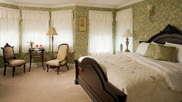A bedroom with a large bed, two chairs, a small table with a lamp, and a picture on the wall.
