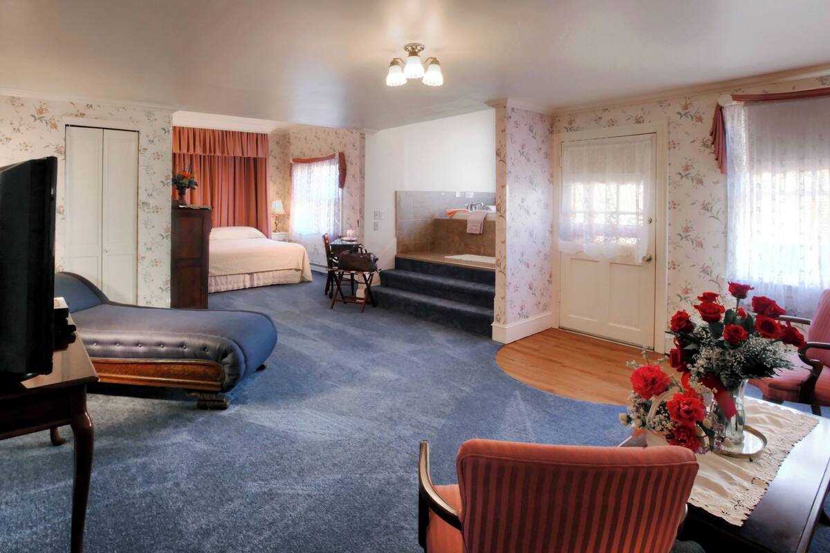 A hotel room with a bed, a TV, a desk with a chair, a bathroom with a sink and shower, and a staircase.