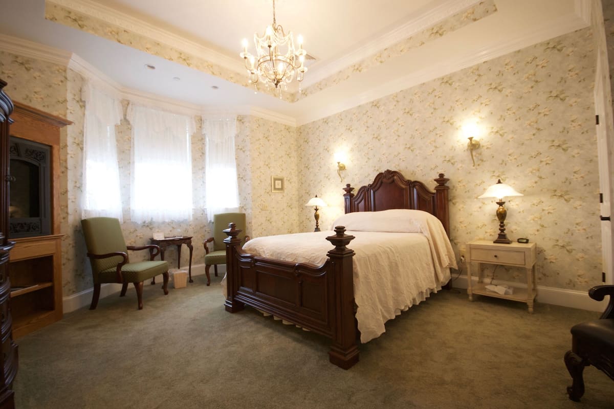 A bedroom with a large bed, two bedside tables with lamps, a chair, a small table, and a dresser.