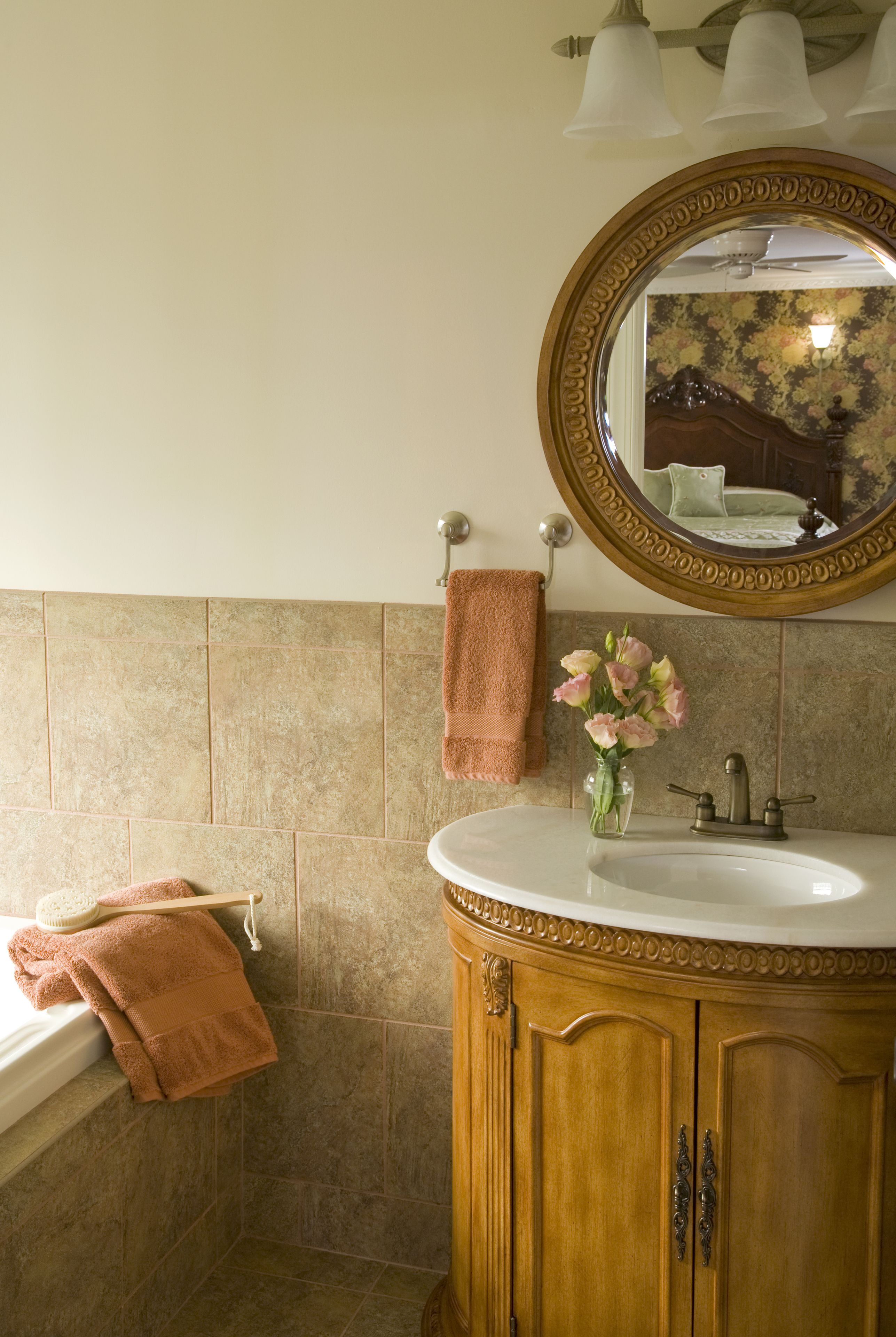 A bathroom with a wooden vanity, a round mirror, and a vase of flowers.