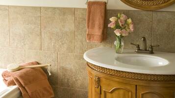 A bathroom with a wooden vanity, a round mirror, and a vase of flowers.