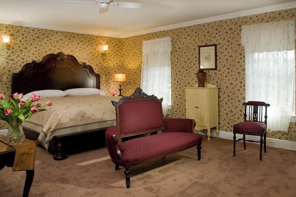 A bedroom with a large bed, two chairs, a dresser, and a cabinet.