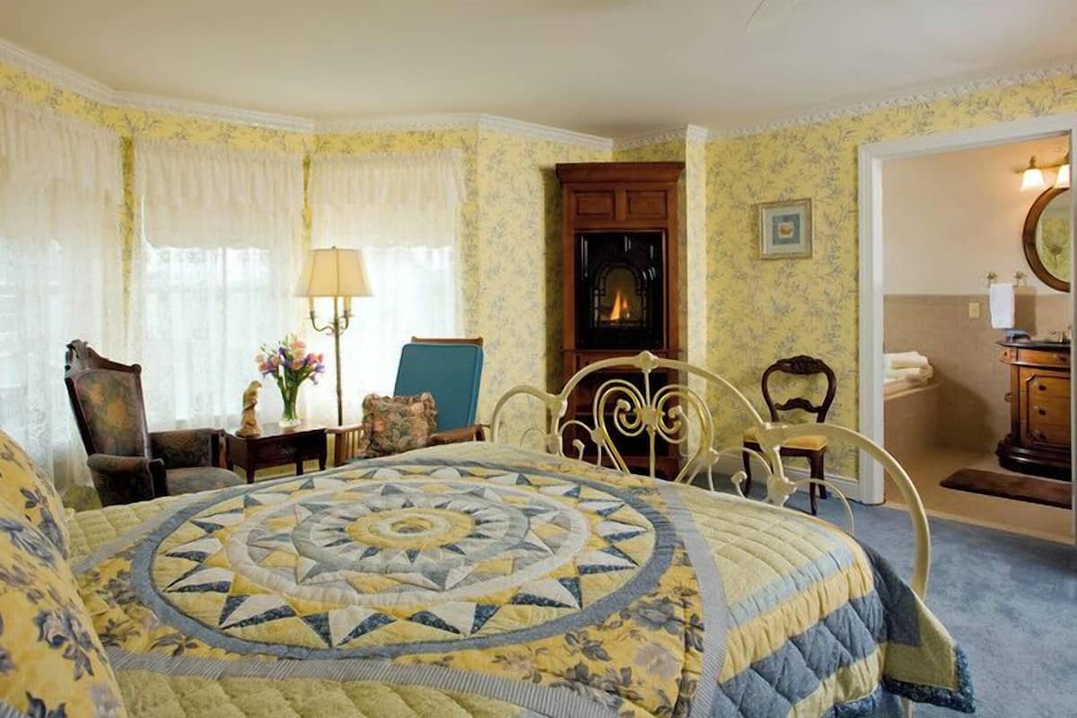 A bedroom with a large bed, a chair, a desk, and a fireplace.