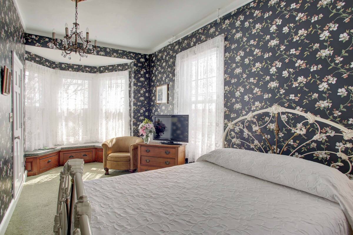 A bedroom with a large bed, a television on a wooden nightstand, a chair, and a chandelier.