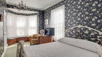 Une chambre à coucher avec un grand lit, un téléviseur posé sur une table de chevet en bois, une chaise et un lustre.