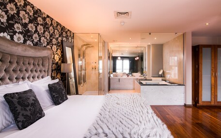 Una habitación de hotel moderna con una cama grande, un baño con ducha y una zona de cocina.