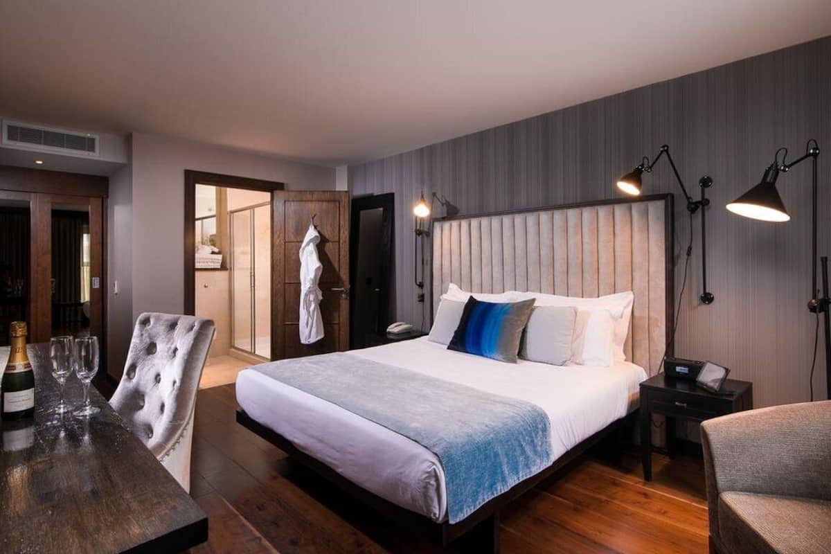 A modern hotel room with a large bed, a wooden desk with a bottle of champagne, and a chair.