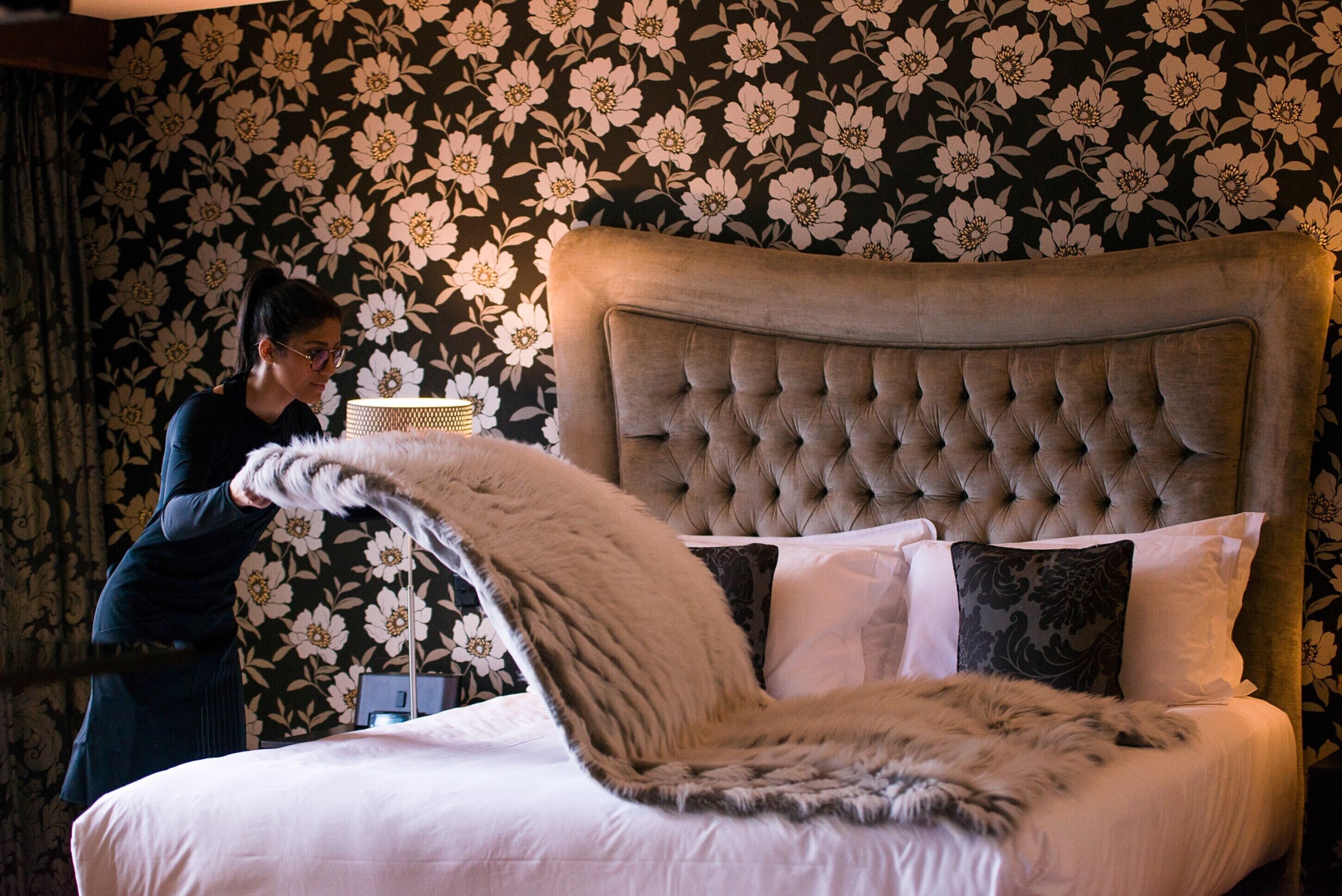 A bed with a tufted headboard, white bedding, and a large fluffy throw.
