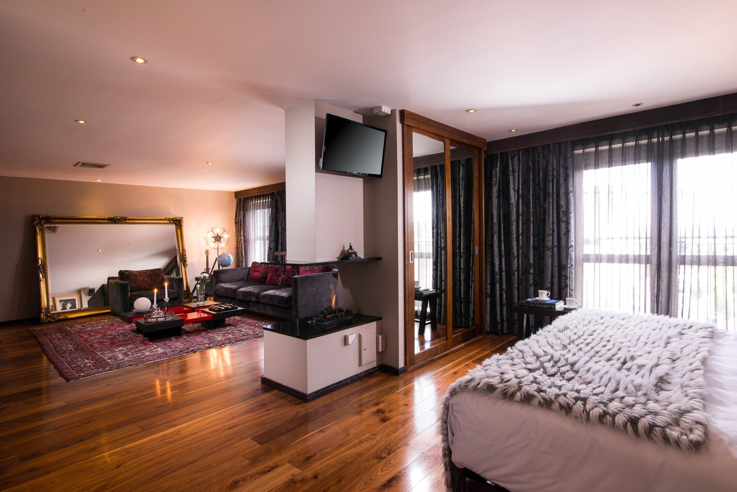 Une chambre d’hôtel moderne dotée d’un grand lit, d’un coin salon avec un canapé et une table basse, d’un téléviseur à écran plat fixé au mur et d’une grande fenêtre avec des rideaux.