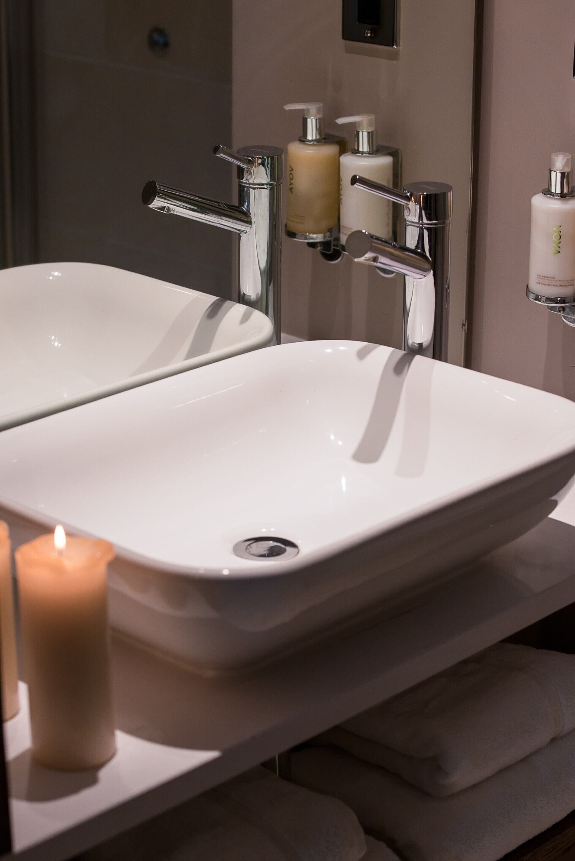 A bathroom with two white sinks, a mirror, and a shelf with toiletries.
