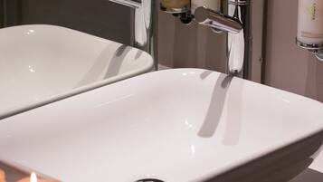 A bathroom with two white sinks, a mirror, and a shelf with toiletries.