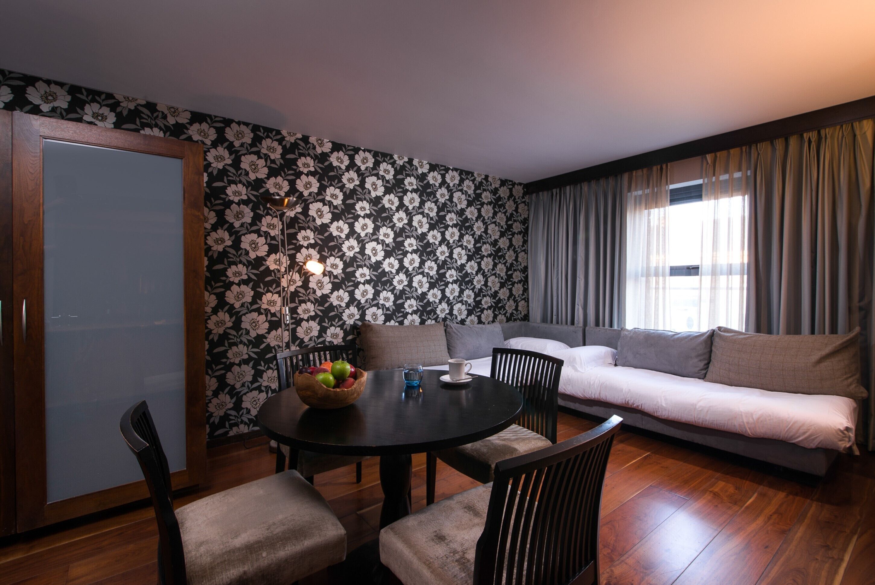 A room with a dining table, chairs, a sofa, and a window with curtains.