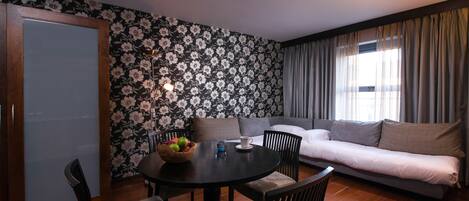 A room with a dining table, chairs, a sofa, and a window with curtains.