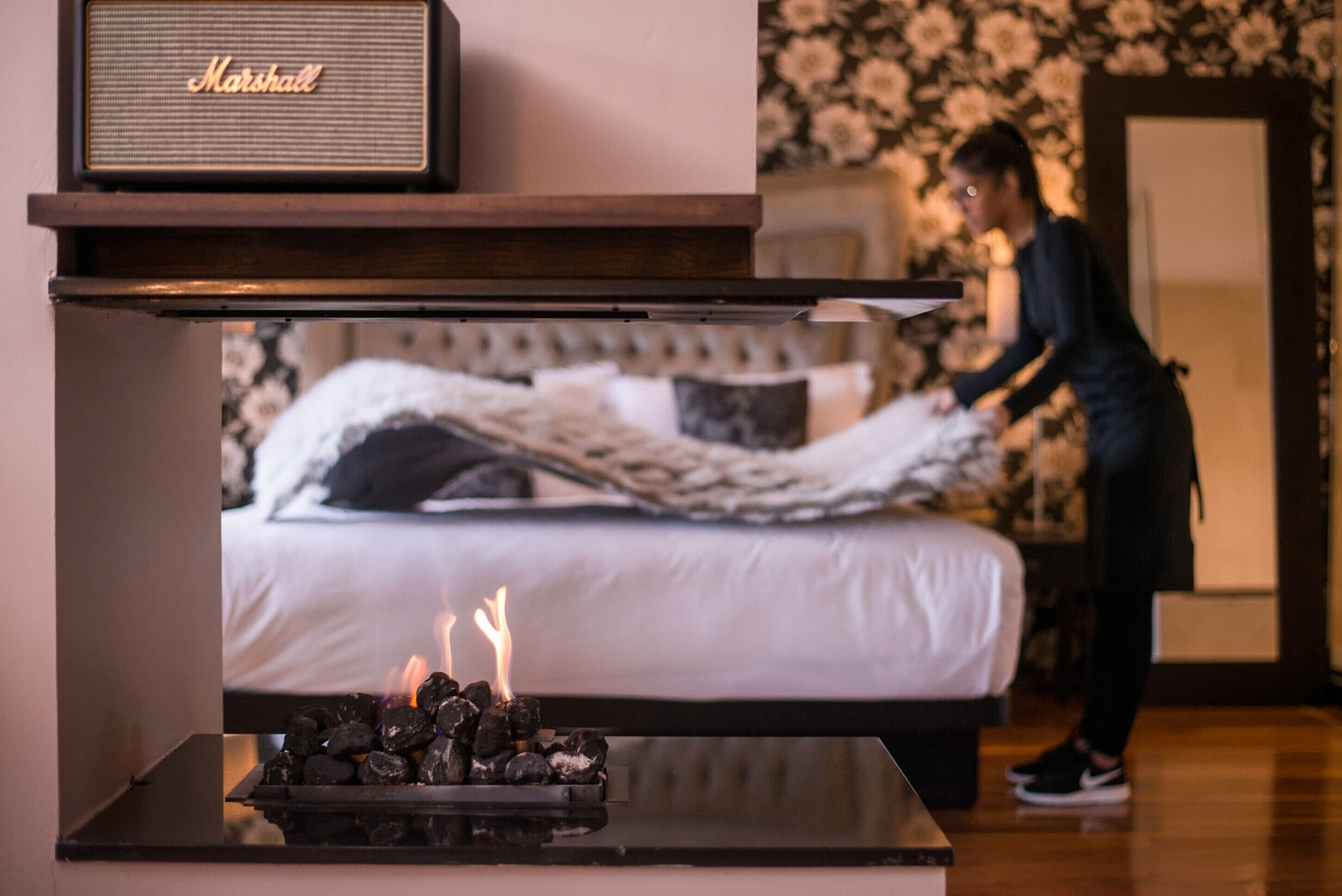 A bedroom with a bed, a radio, and a fireplace with burning logs.