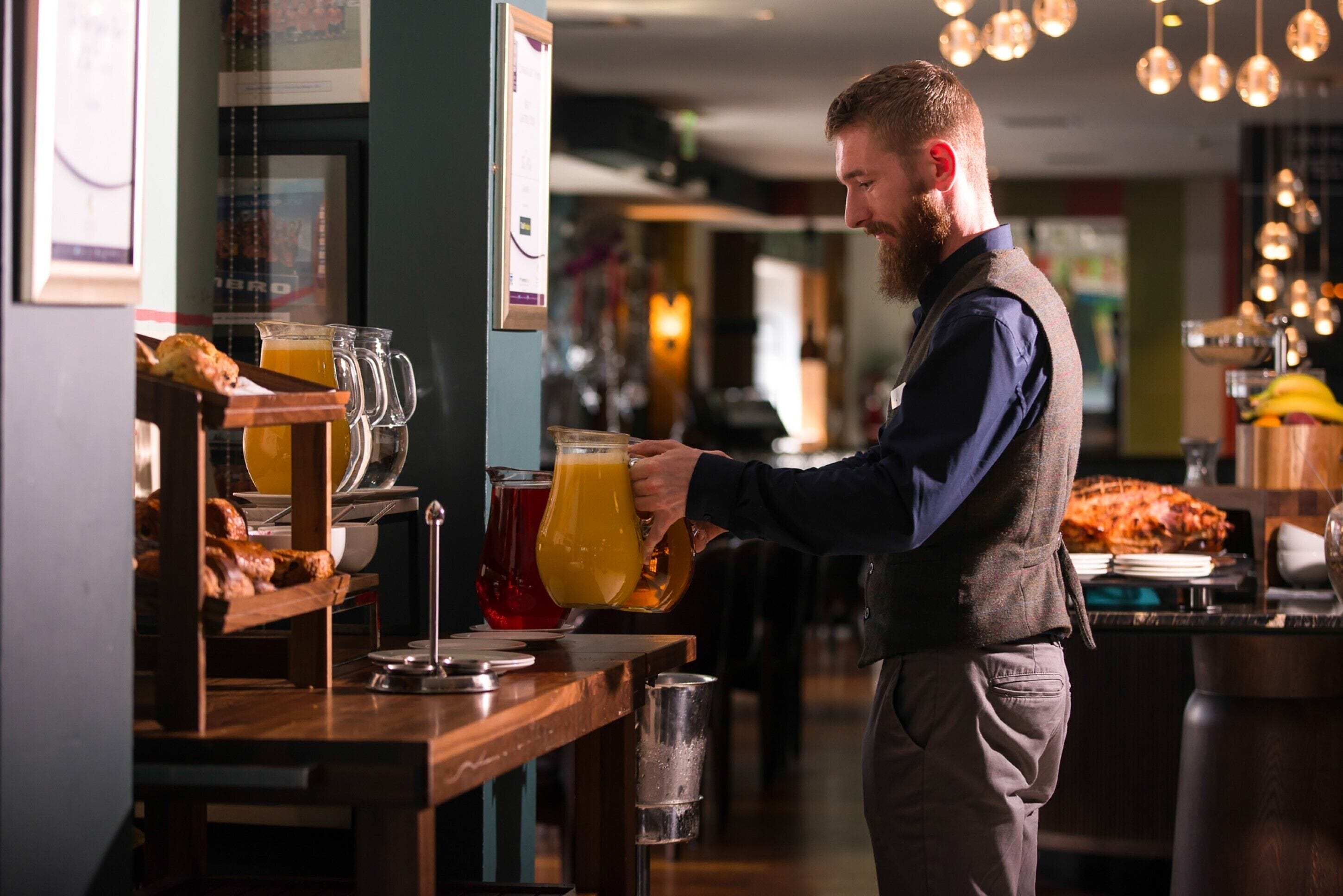 A bar area with a counter, a person pouring a drink, and a display of bread and fruit.