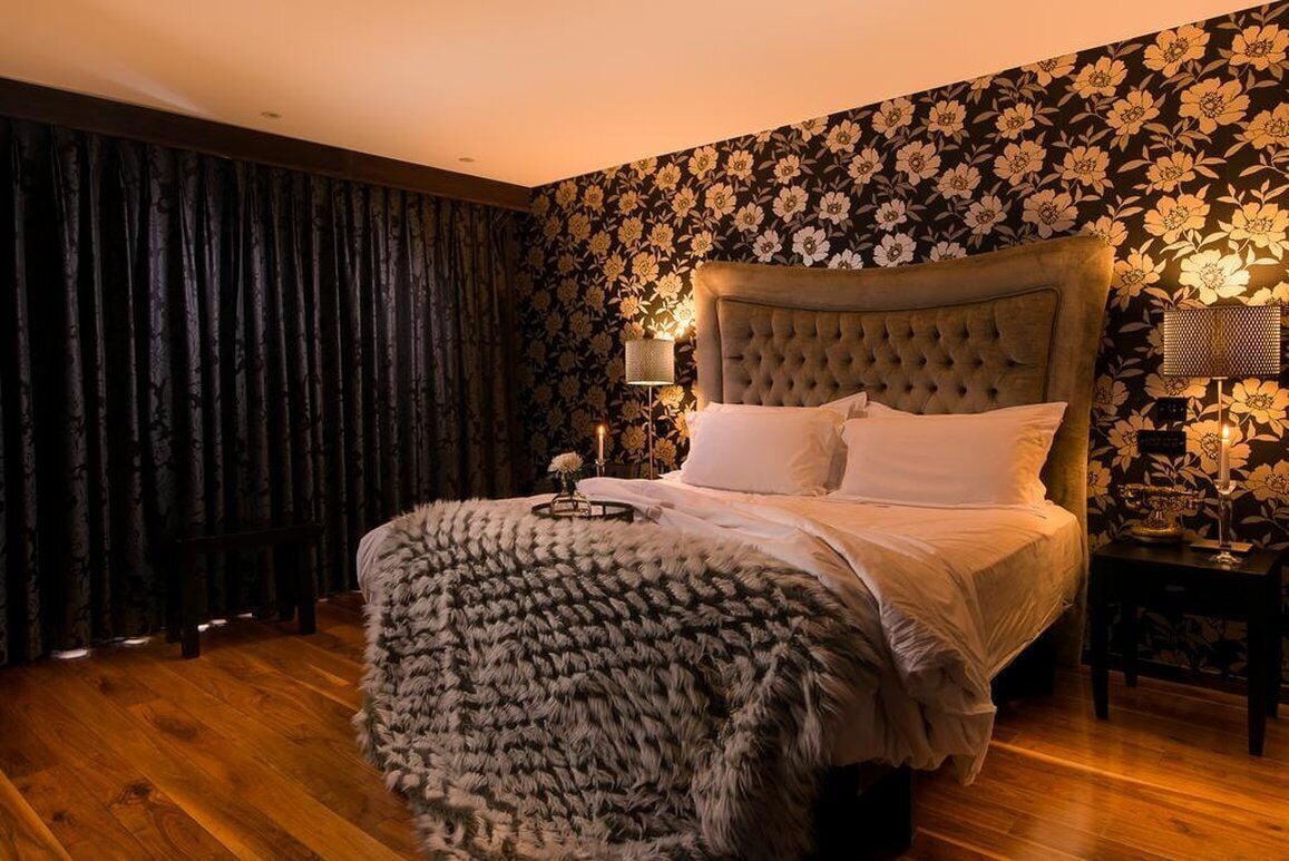 A bedroom with a tufted headboard, a fluffy throw blanket, and a floral wallpaper.