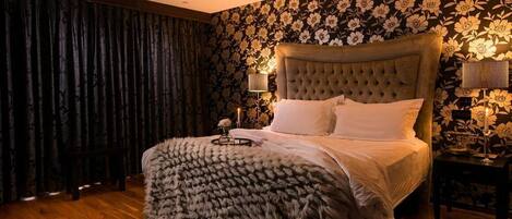 A bedroom with a tufted headboard, a fluffy throw blanket, and a floral wallpaper.