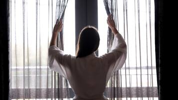Una persona dret davant d'una finestra amb cortines primes, subjectant-les.