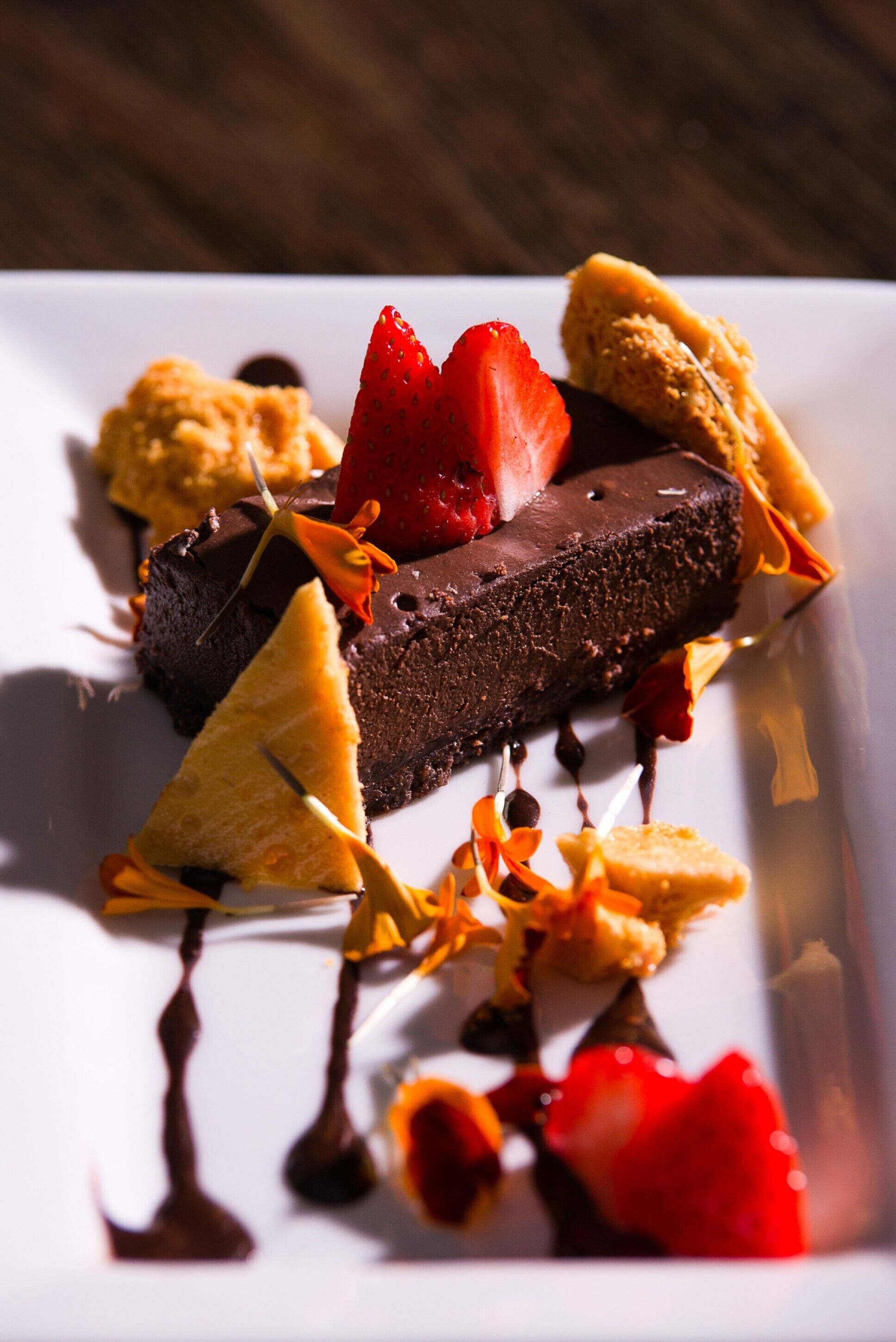 A dessert on a white plate with chocolate, strawberries, and caramelized sugar.