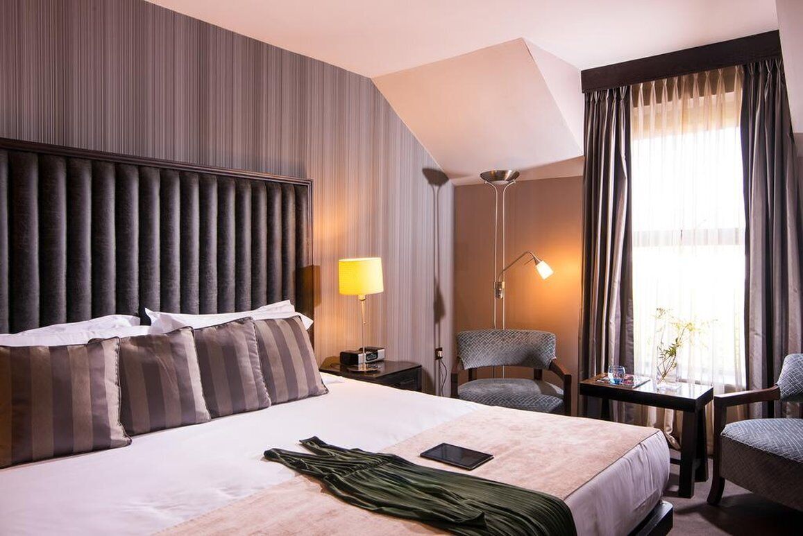 A hotel room with a large bed, a desk, a chair, and a lamp.