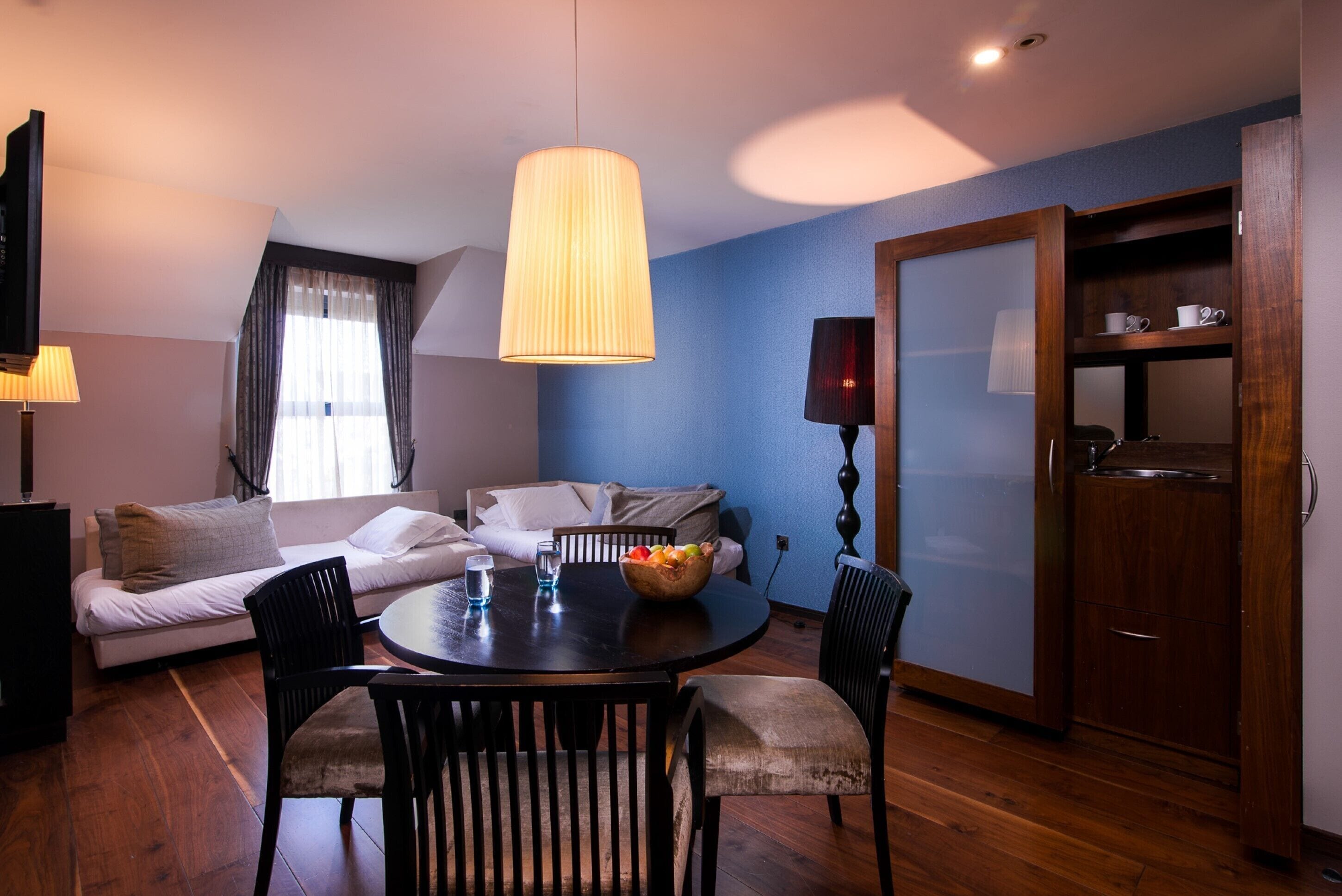 A modern living room with a sofa, dining table, and chairs, a large window with curtains, and a wooden cabinet.