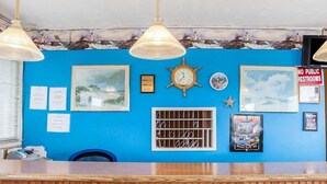 A reception desk with a blue wall, framed pictures, a clock, and a sign prohibiting public restrooms. - Rodeway Inn & Suites (Long Beach)