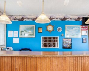 A reception desk with a blue wall, framed pictures, a clock, and a sign prohibiting public restrooms. - Rodeway Inn & Suites (Long Beach)