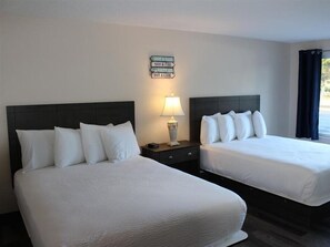 A hotel room with two beds, a nightstand with a lamp, and a sign on the wall. - Rodeway Inn & Suites (Long Beach)