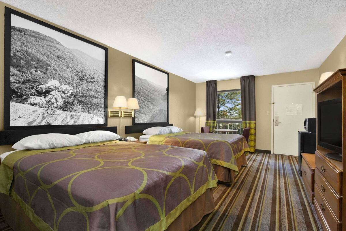 Een hotelkamer met twee bedden, een televisie, een bureau en een raam met gordijnen.
