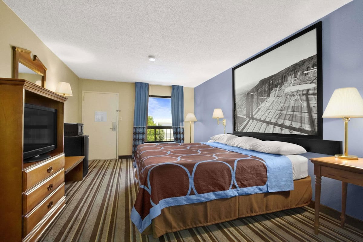 Een hotelkamer met een bed, een televisie, een bureau en een groot raam met gordijnen.