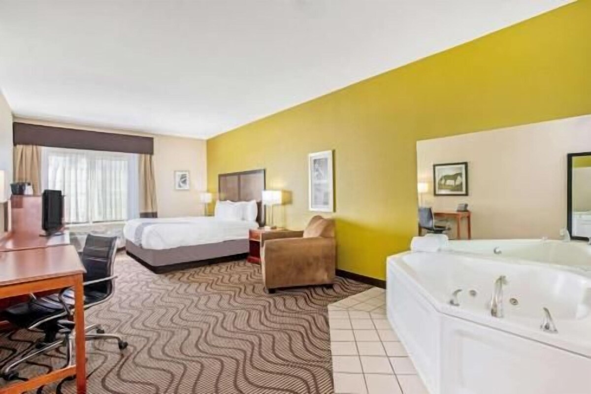 Een hotelkamer met een bed, een bureau, een stoel, een bank, een badkuip en een raam met gordijnen.