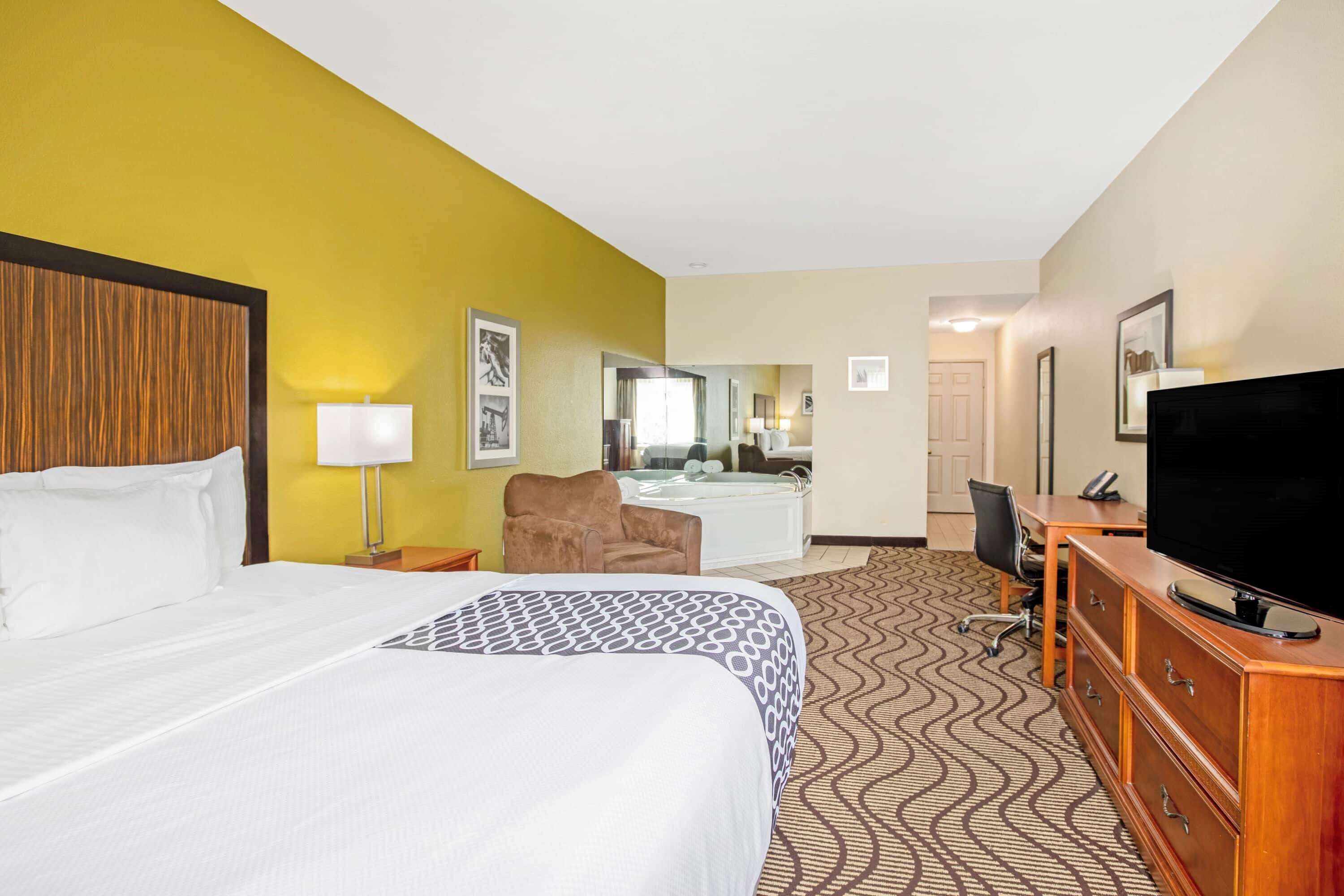 A hotel room with a bed, a desk, a chair, a television, and a bathroom with a bathtub.