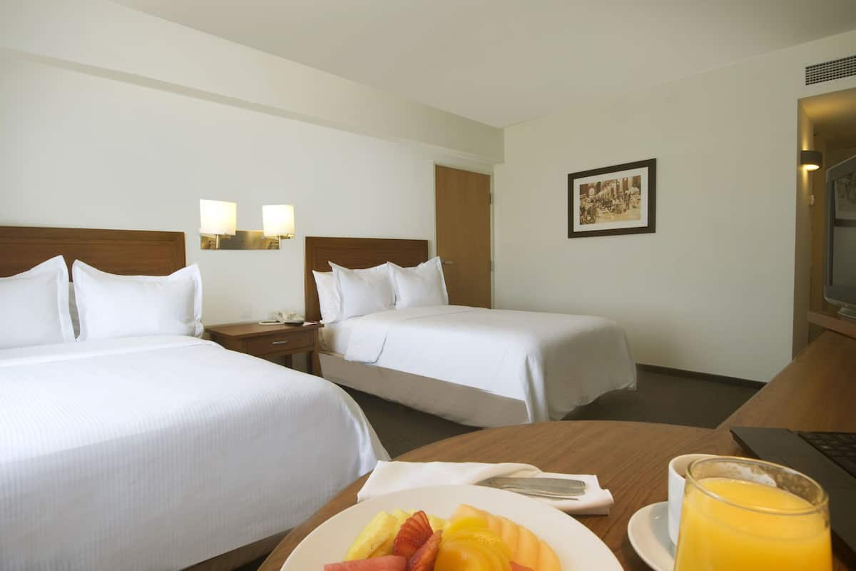 A hotel room with two beds, a dining table with breakfast, a laptop, and a framed picture on the wall.
