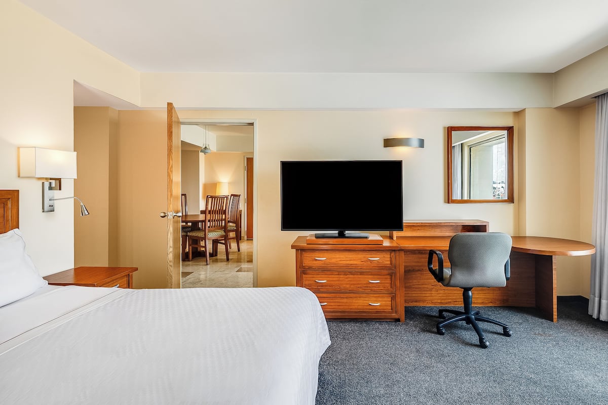 A hotel room with a bed, a desk with a TV, a chair, and a mirror.