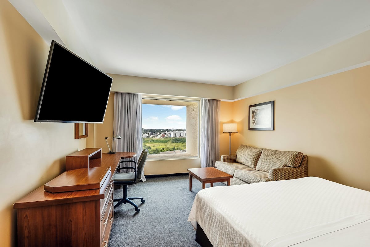A hotel room with a bed, desk, chair, and a TV mounted on the wall.